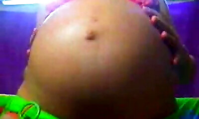 एक गर्भवती श्यामला तंग नीयन बिकनी में पहने और उसके बड़े माँ स्तन चमकती है